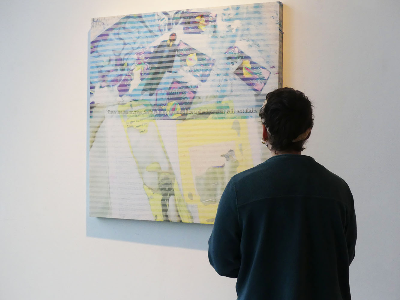 Person standing before a colorful abstract digital painting with blue, yellow, and purple shapes; text on the artwork reads, 'Your work may be highly admired by your peers but will not last.'