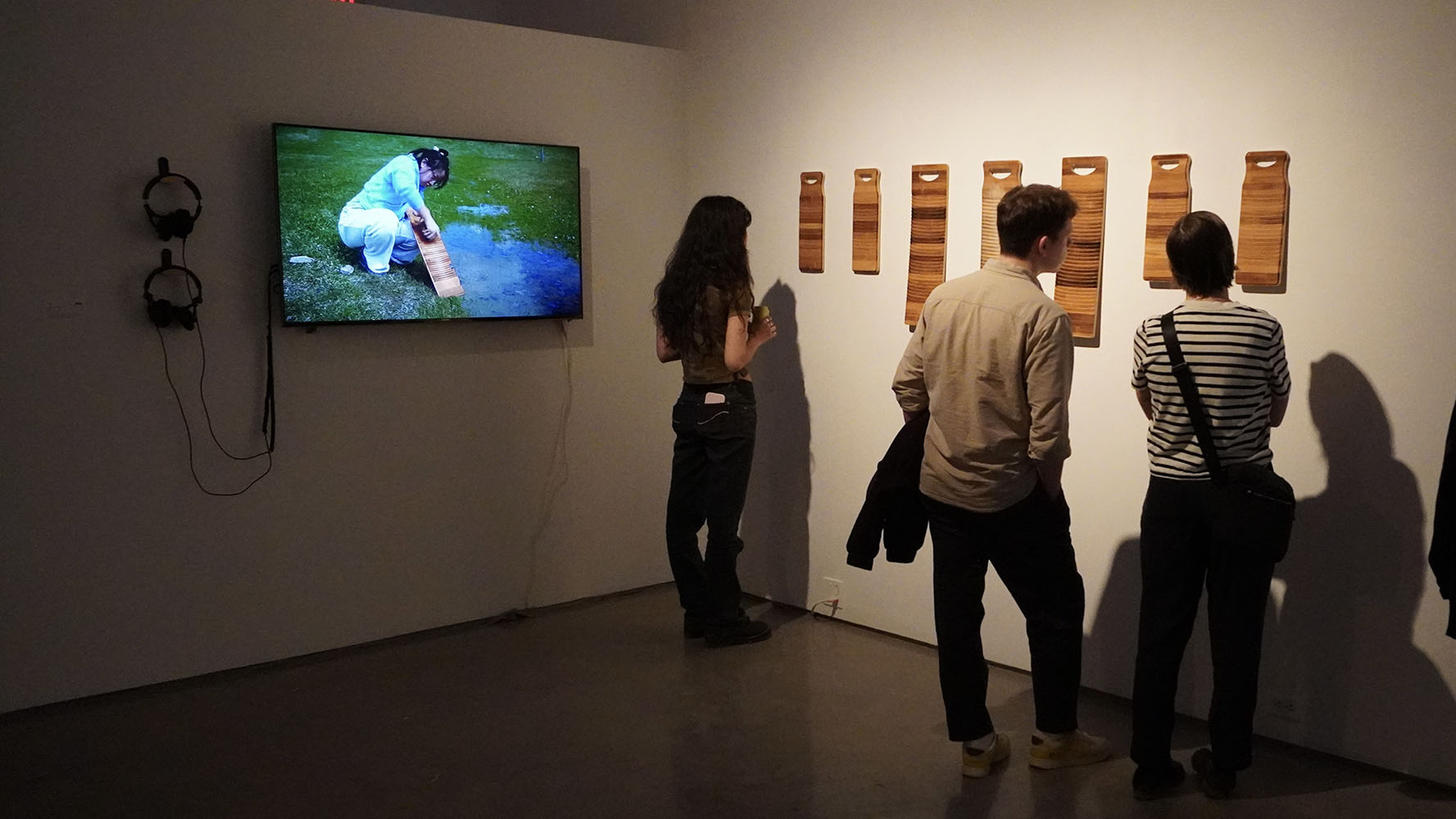 Three people viewing a video of river laundry alongside wooden washboards in an art exhibit.