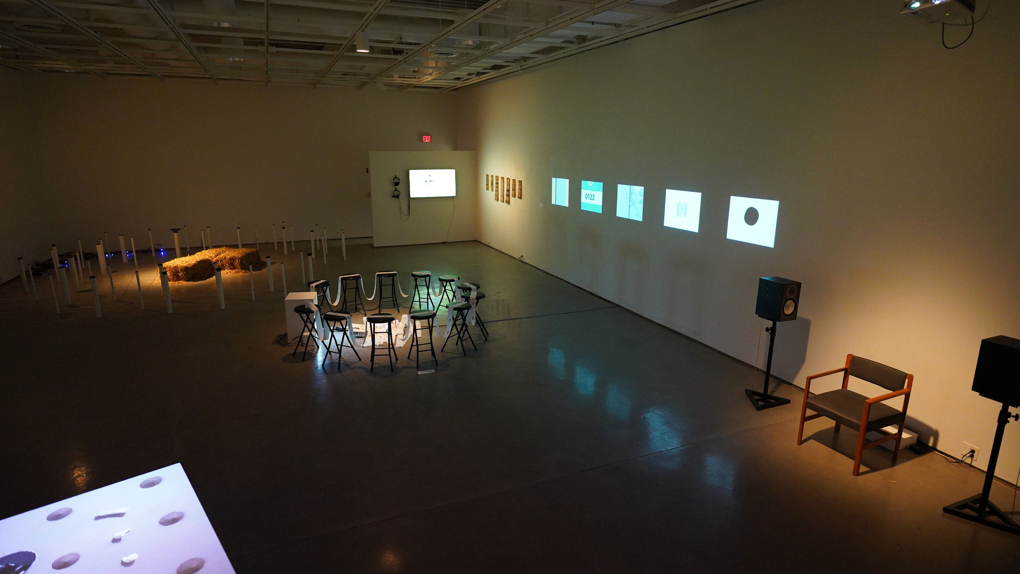 Gallery wall with five projected images and stools arranged in front.