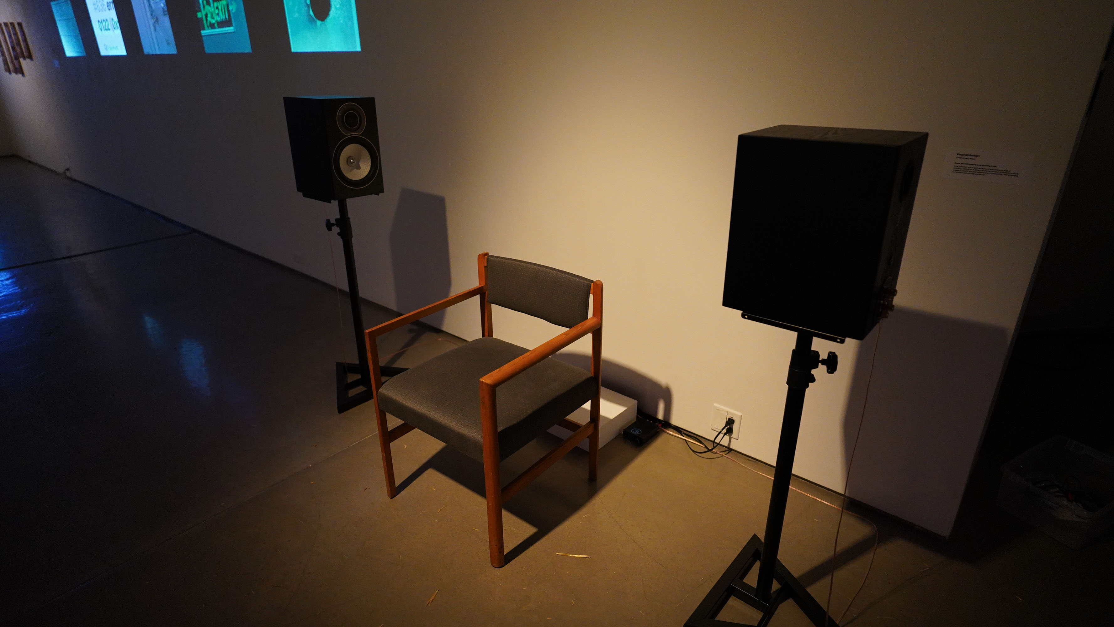 Single chair positioned between two speakers in a gallery.