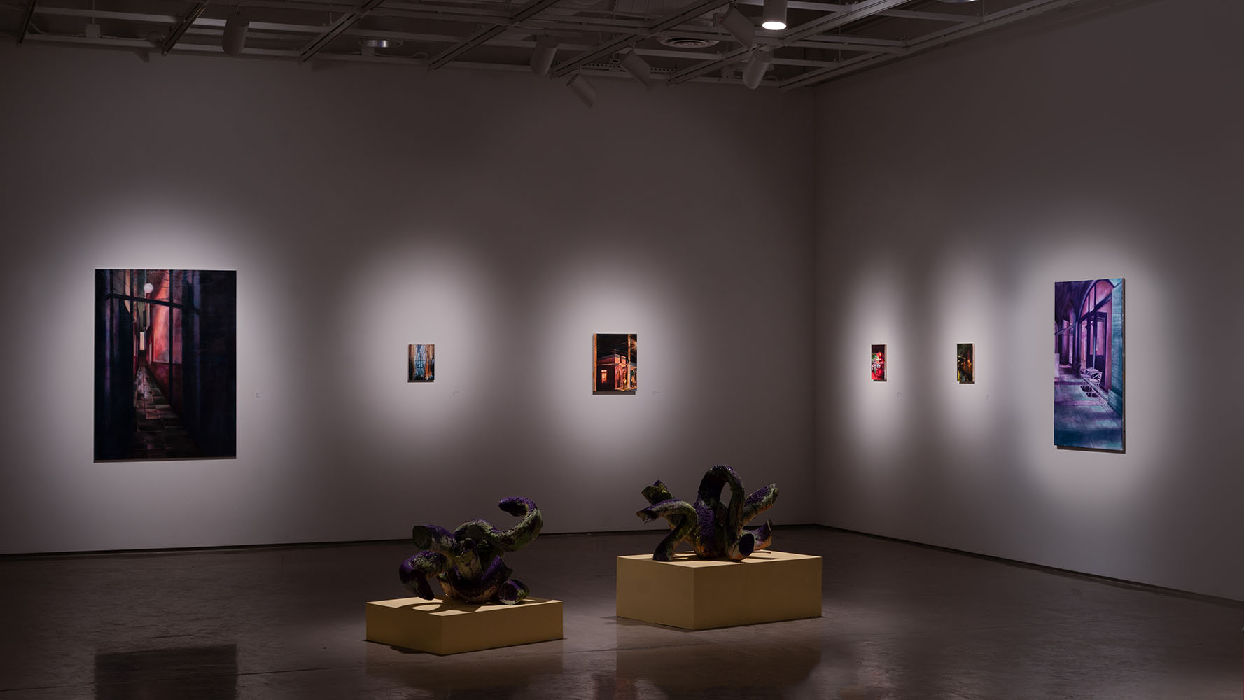Dimly lit gallery room displaying paintings and sculptures.