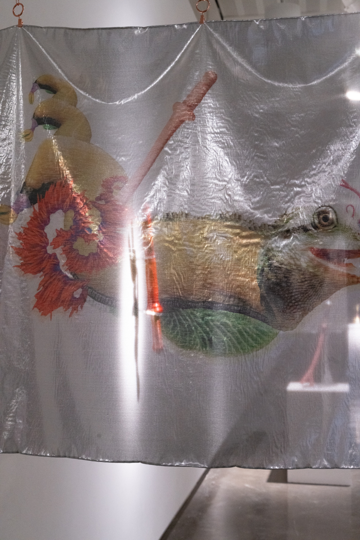A translucent fabric artwork suspended from the ceiling, featuring flowers and an animal head.