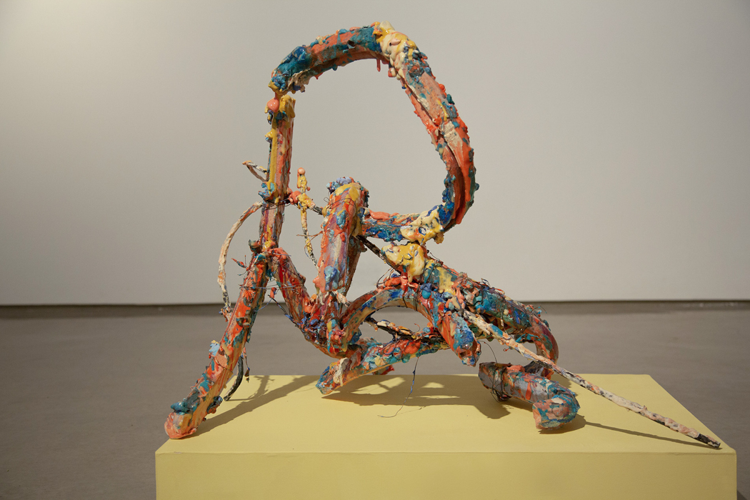 Colorful abstract sculpture with looping forms on a yellow pedestal.
