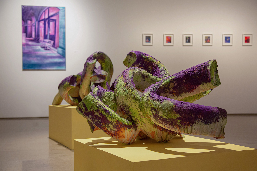 Two vibrant twisted sculptures on yellow pedestals with artwork in the background.