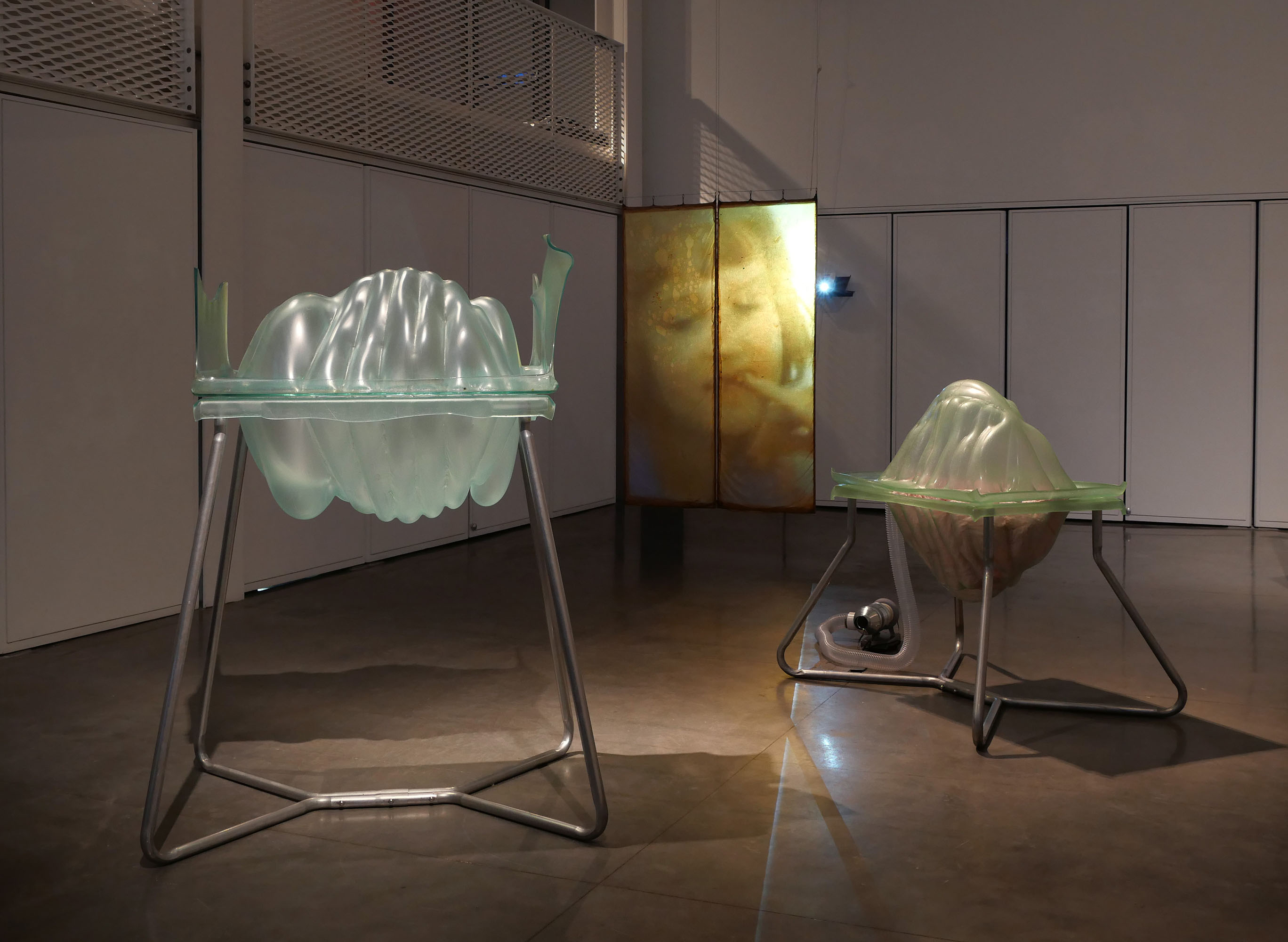 Two translucent sculptures on stands with a projected face in the background.