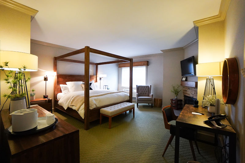 poster bed with white linens, fireplace and armchair by window