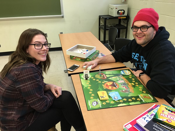 Two students smile while playing a colorful board game during a psychology or art therapy class activity.