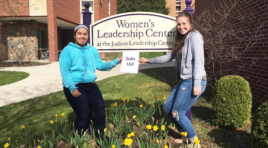 Two ladies posing in front of the Women's leadership sign