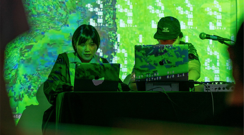 Photo of elekhlekha อีเหละเขละขละ, two indiuals in green light over a computer